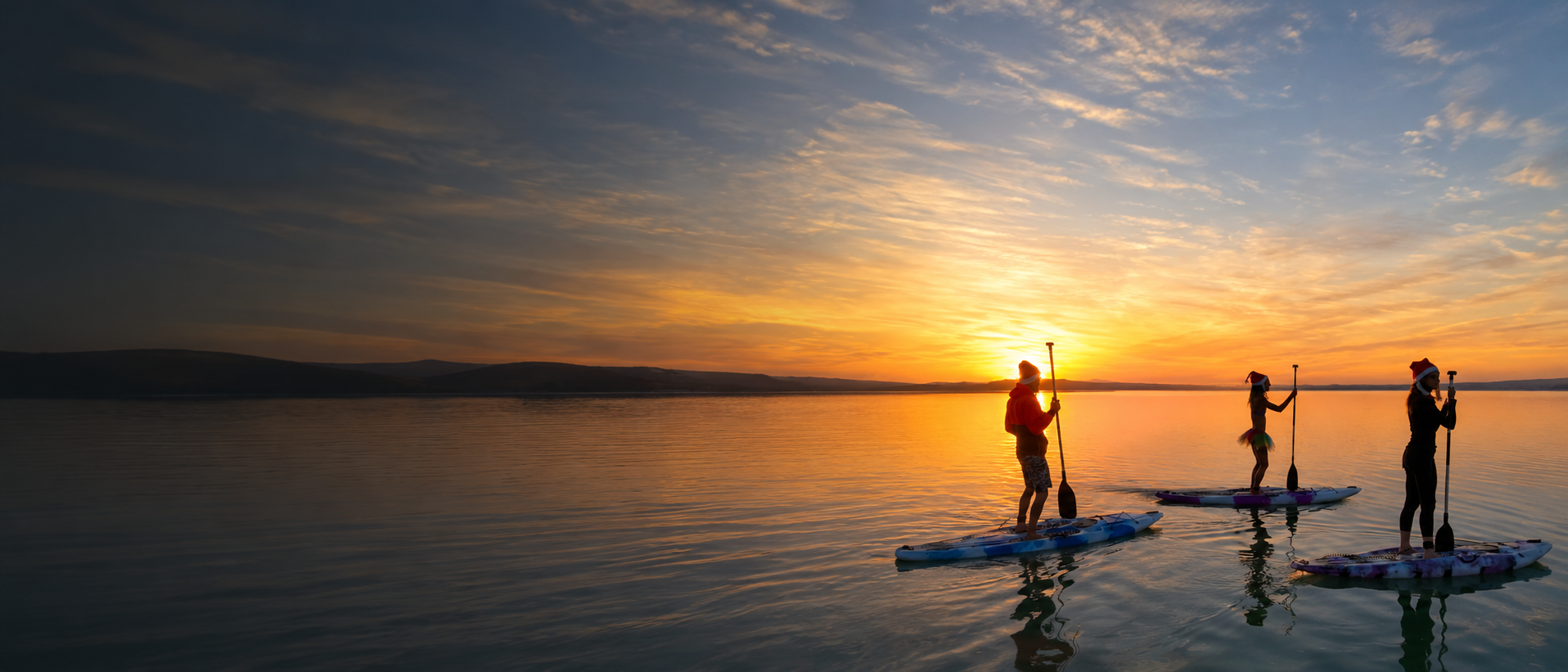 Group enjoying stand-up paddleboarding on calm water at sunset in Langebaan