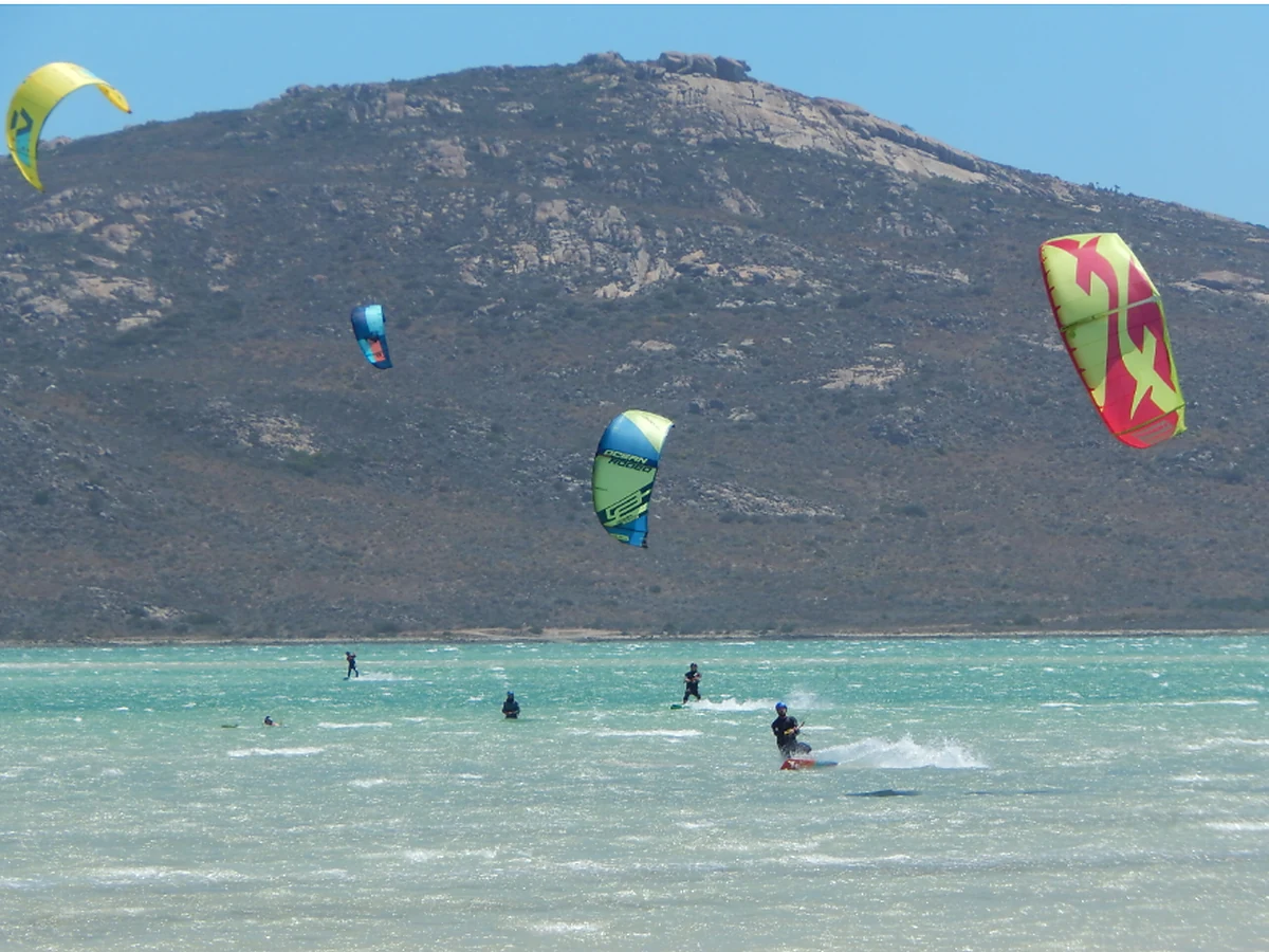 Kitesurfers riding on the Langebaan lagoon with the West Coast landscape behind them